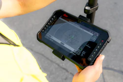Worker in yellow safety vest holding rugged tablet displaying surveying or mapping software outdoors