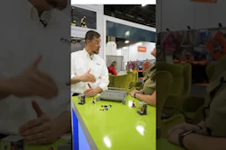 Man demonstrating robotics project at bright green table during technology exhibition event