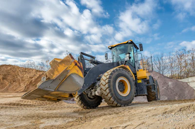 Yellow and black wheel loader with full bucket on sandy construction site under blue sky