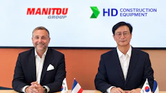 Two business executives at a formal meeting with Manitou Group and HD Construction Equipment logos, French and South Korean flags on table