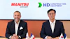 Two business executives at a formal meeting with Manitou Group and HD Construction Equipment logos, French and South Korean flags on table
