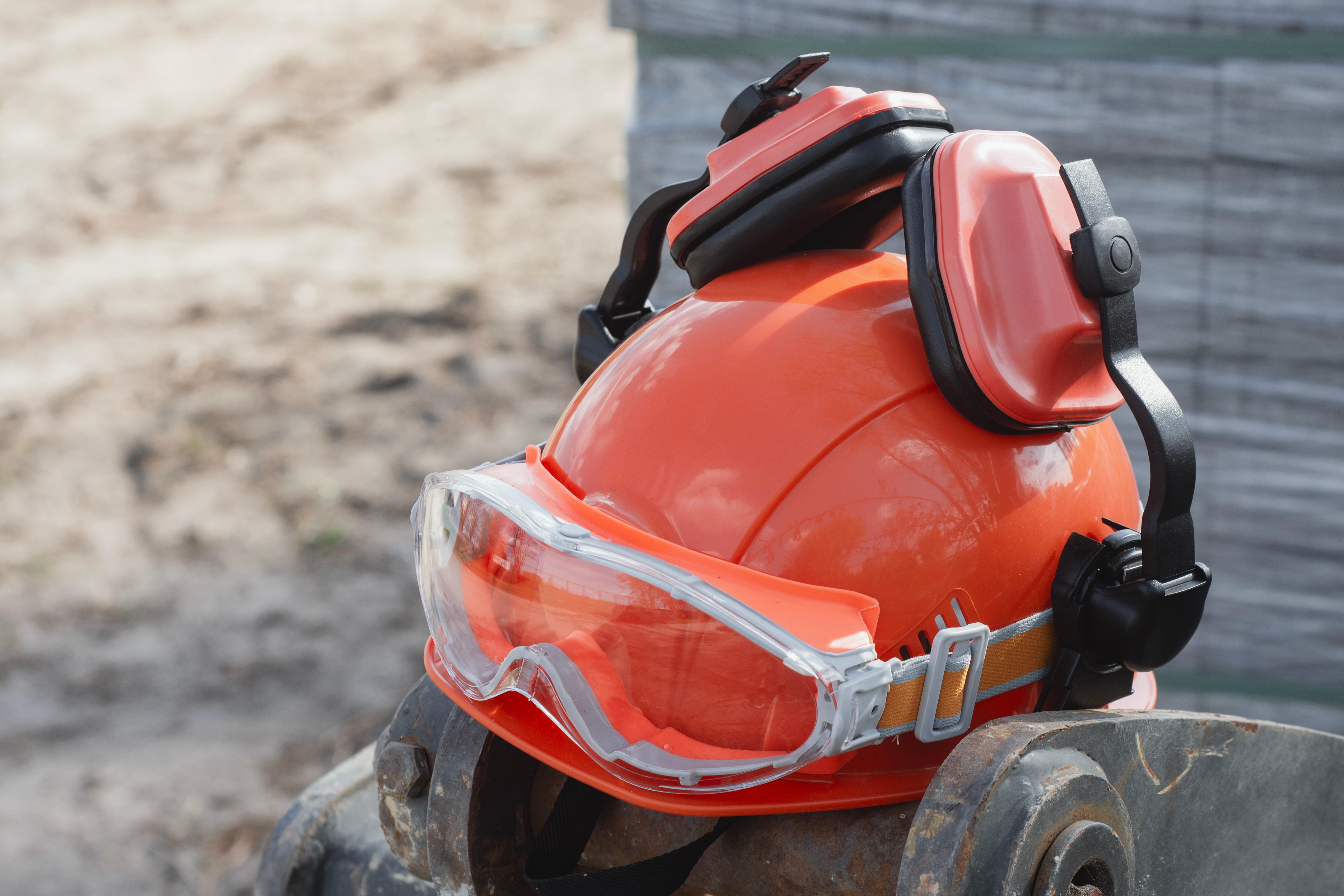 Orange safety hard hat with reflective stripes and protective goggles on a tire at a construction site
