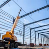 Mobile crane lifting steel beams at industrial construction site with metal framework