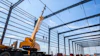 Mobile crane lifting steel beams at industrial construction site with metal framework