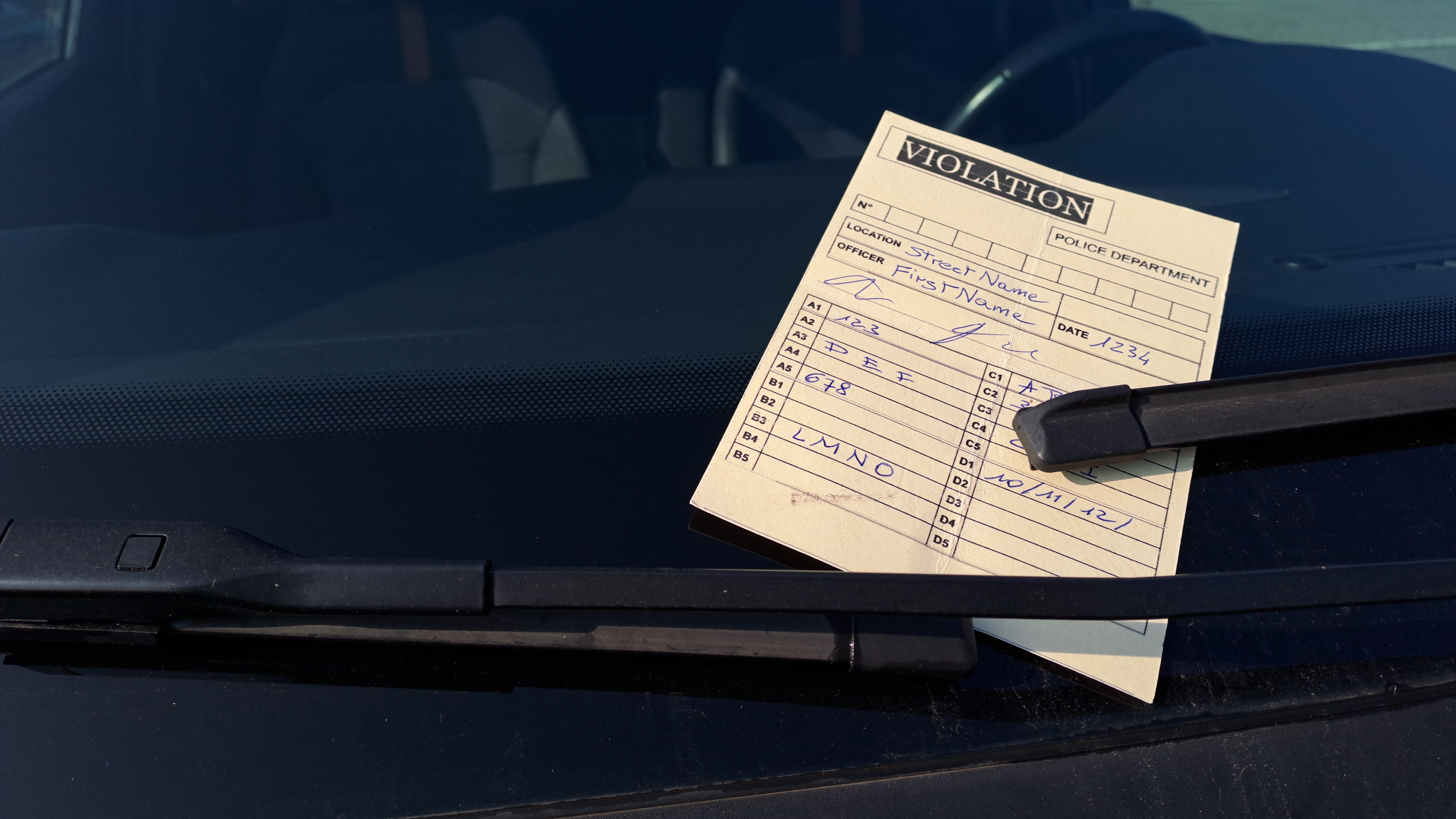 Parking violation ticket placed under windshield wiper blade on dark vehicle