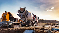 Concrete mixer truck and yellow pump truck operating on construction site with rural landscape