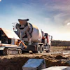 Concrete mixer truck and yellow pump truck operating on construction site with rural landscape