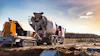 Concrete mixer truck and yellow pump truck operating on construction site with rural landscape