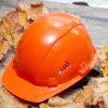 Bright orange safety hard hat surrounded by dried autumn leaves on weathered wood