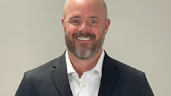 Professional headshot of a smiling man in dark blazer and white shirt against neutral background