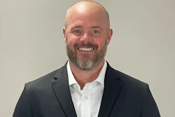 Professional headshot of a smiling man in dark blazer and white shirt against neutral background