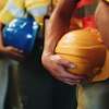 Construction workers in safety vests holding yellow, blue, and white hard hats during a team meeting