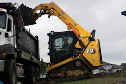 Yellow CAT skid steer loader loading gravel into white dump truck on construction site