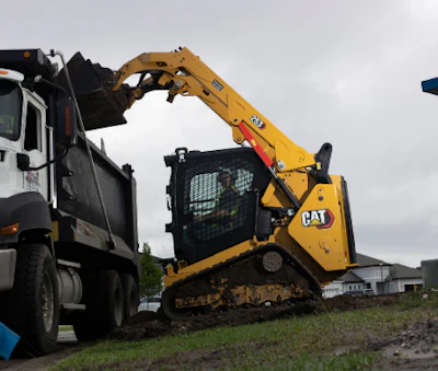 Yellow CAT skid steer loader loading gravel into white dump truck on construction site