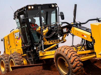 Yellow Caterpillar motor grader with black cab and large tires on dirt surface