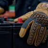 Close-up of tan and black tactical work gloves with textured grip pattern worn during hands-on task