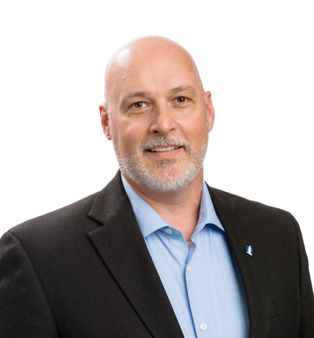 Professional headshot of a bald man with gray beard wearing a black blazer and light blue shirt