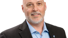 Professional headshot of a bald man with gray beard wearing a black blazer and light blue shirt
