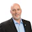 Professional headshot of a bald man with gray beard wearing a black blazer and light blue shirt Headshot