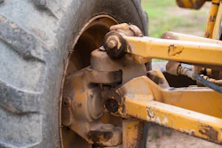 Close-up of rusted wheel hub and axle assembly on heavy construction equipment with yellow metal frame