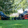 Yellow and red landscaping compactor equipment displayed on grass with trees in background