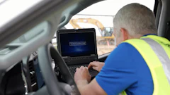 Construction worker in safety vest using Toughbook laptop in vehicle at job site