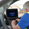 Construction worker in safety vest using Toughbook laptop in vehicle at job site