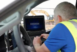 Construction worker in safety vest using Toughbook laptop in vehicle at job site