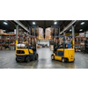 Two yellow and black forklifts operating in an industrial warehouse with shelving and pallets