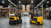 Two yellow and black forklifts operating in an industrial warehouse with shelving and pallets