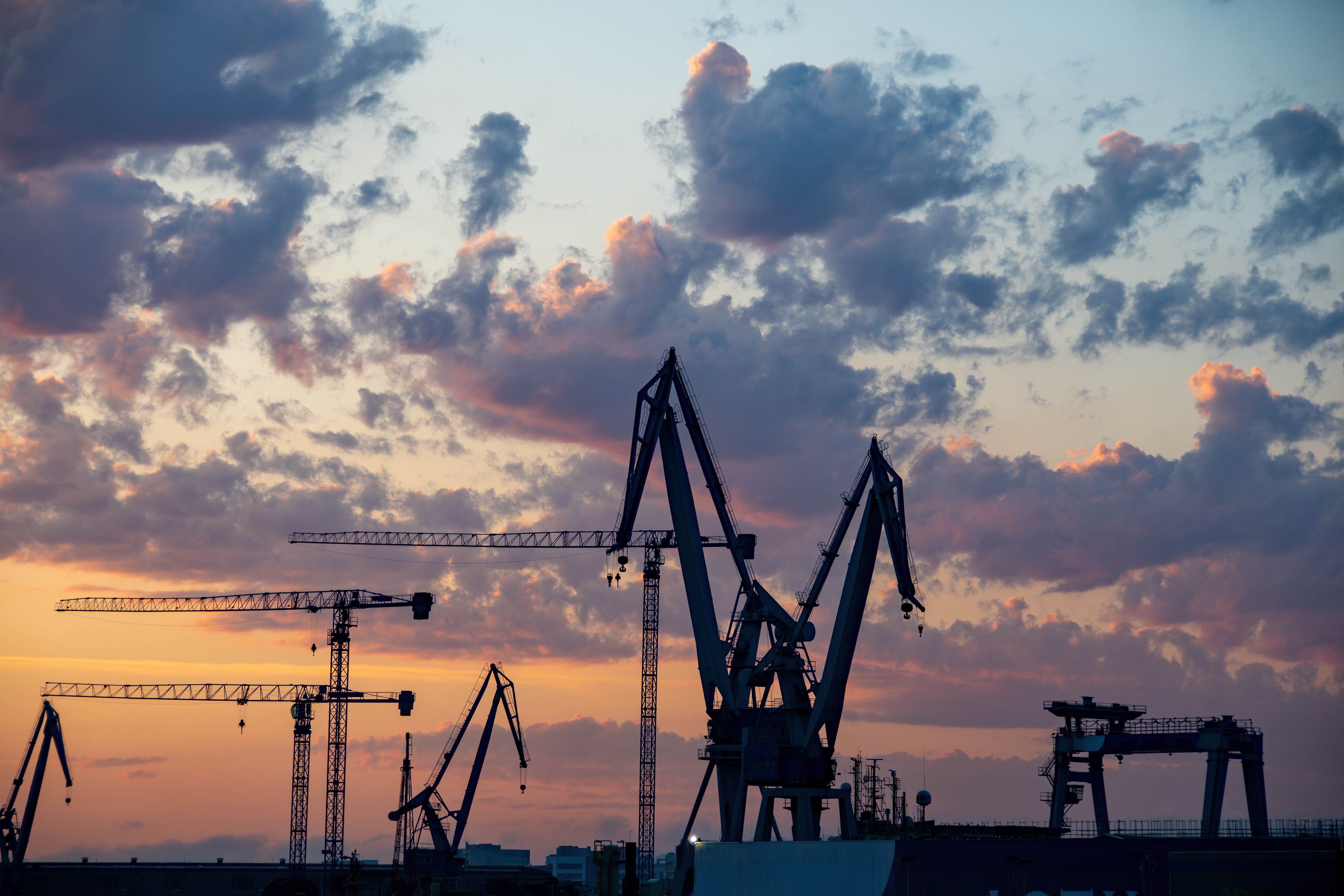 Industrial port cranes silhouetted against a dramatic sunset sky with orange and blue clouds
