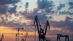Industrial port cranes silhouetted against a dramatic sunset sky with orange and blue clouds