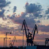 Industrial port cranes silhouetted against a dramatic sunset sky with orange and blue clouds