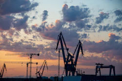 Industrial port cranes silhouetted against a dramatic sunset sky with orange and blue clouds