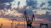 Industrial port cranes silhouetted against a dramatic sunset sky with orange and blue clouds
