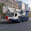 White and blue Tadano mobile crane truck parked on urban street with city buildings in background