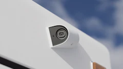 White dome security camera mounted on exterior surface with blue sky background