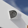 White dome security camera mounted on exterior surface with blue sky background