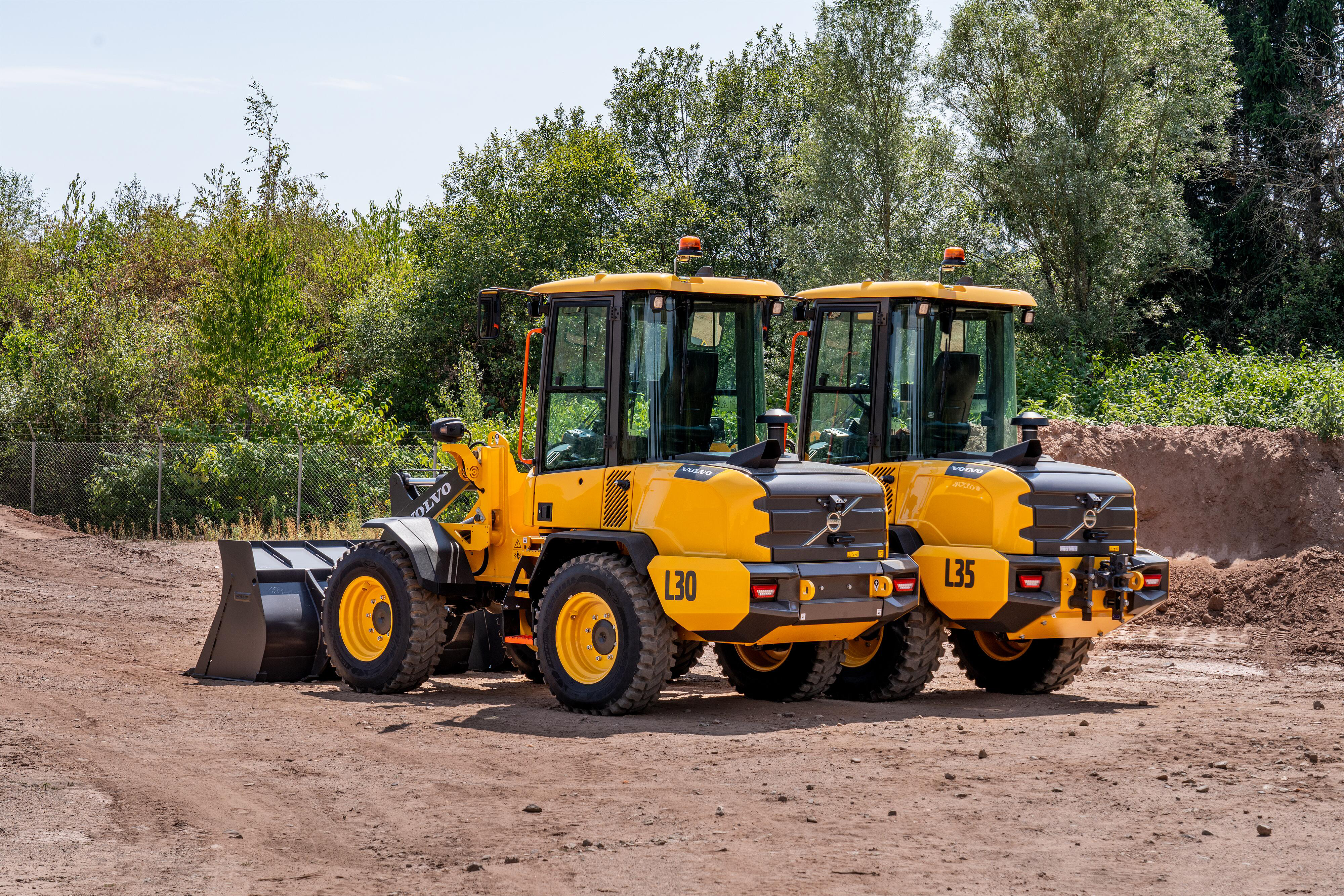 Yellow Volvo wheel loader and vibratory rollers parked on construction site with trees in background