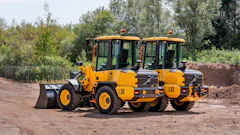 Yellow Volvo wheel loader and vibratory rollers parked on construction site with trees in background