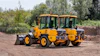 Yellow Volvo wheel loader and vibratory rollers parked on construction site with trees in background