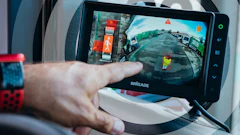 Person holding Brigade dashcam displaying wide-angle vehicle footage with traffic scene