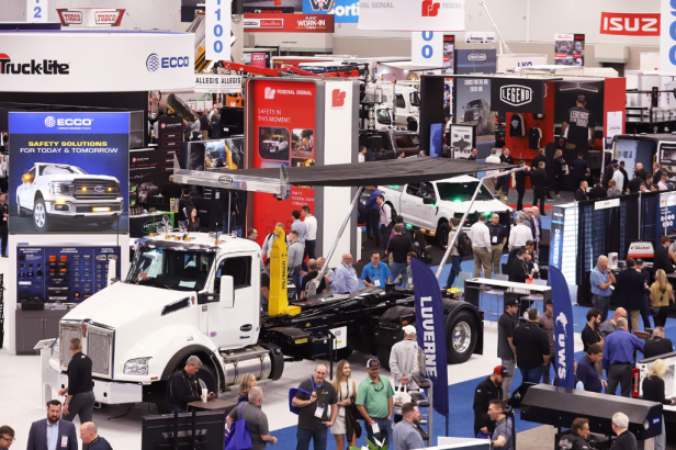 Busy trade show floor with white commercial truck display and multiple vendor booths showcasing automotive and truck equipment brands.