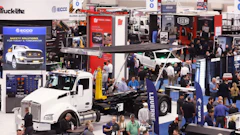 Busy trade show floor with white commercial truck display and multiple vendor booths showcasing automotive and truck equipment brands.