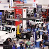 Busy trade show floor with white commercial truck display and multiple vendor booths showcasing automotive and truck equipment brands.