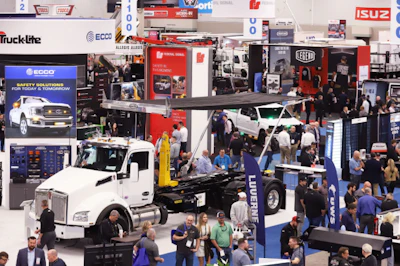 Busy trade show floor with white commercial truck display and multiple vendor booths showcasing automotive and truck equipment brands.